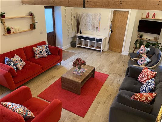 Sitting room with a dark grey sofa on the right. On the left is a bright red sofa, in the  centre is a wooden coffee table with fresh flowers on it.  There is rug that matches the colour of the red sofa.